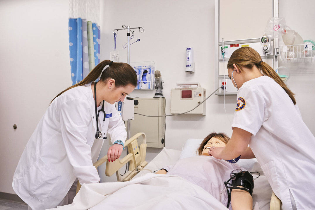 Two nursing students take pulse in nursing lab